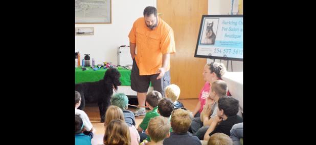 CCLP/LYNETTE SOWELL - Kids from First Step Child Care listen to Sam Guinn, owner of Barking Oaks Pet Salon. Pebble, Guinn’s Standard Poodle, was there as well to provide an object lesson on pets for the children. First Presbyterian Church hosted the day care center at its Day for Dogs, Cats and Kids on Wednesday.