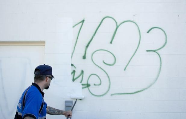 Senior code compliance officer, Beau Brabbin, paints over a gang tagging left on the rear of Mighty Mart Jan. 28. With the help of volunteers the tagging and profanity were covered at no cost to the store that opened at the end of 2013.