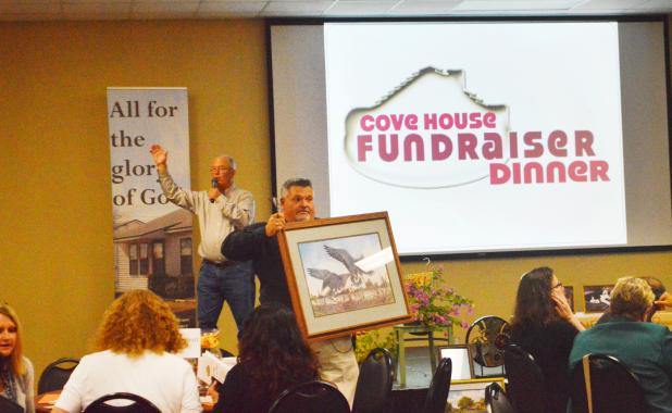 CCLP/LYNETTE SOWELL - Brian Hawkins, executive director of Cove House holds up a framed print during the live auction as he helps raise money for the homeless shelter and free clinic Monday evening
