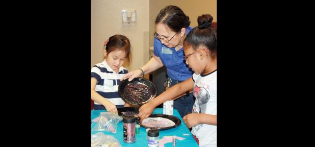 CCLP/KATHLEEN STARLING - Carroll Beckom helps students add glitter stars to their spiral galaxies before they turn them into mobiles at CTC’s College for Kids Galaxy Quest class last Wednesday.
