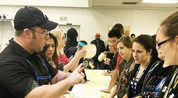 COURTESY PHOTO - Domino’s Pizza assistant manager Michael Bouvier shows a Crossroads High School student how to get air underneath to dough to allow it to spread out as it is tossed into the air. Domino’s presented its Dough Show at the high school of choice to allow students to explore a career in culinary arts.