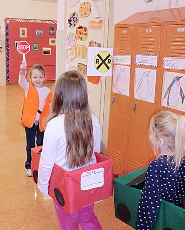 Safety Guard Gracelynn Newton, a kindergarten student at Martin Walker Elementary, stops drivers Madelynn Gorres and Zoe Murray in the hallway. School faculty redesigned the hallway to replicate a roadway with a striped white line, a rotating stop light and crossing guards teaching students not only the rules of the road but also how to enforce them.