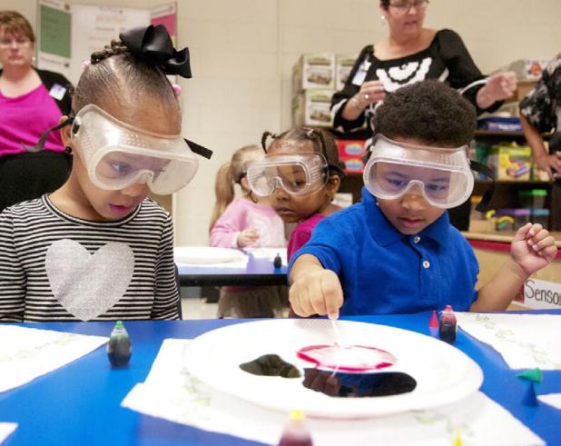 Israel Hagger dips his Q-tip covered with soap into the food coloring as Nevaeh Lewis watchs the reaction