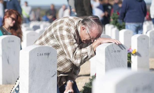 Bruce Ellyson kneels at the stone of his wife during the wreath placement Saturday in Killeen. Thousands of volunteers gathered for the 10th annual event, decorating more than 5,000 veteran’s headstones in the Central Texas State Veterans Cemetery.