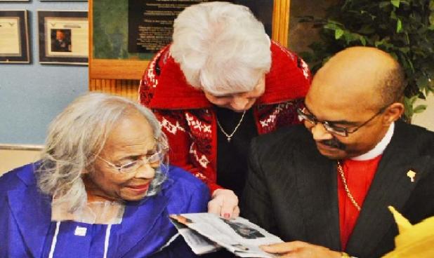 Barbara Burke, one of Alither Mae Stephens’ Golden Girl bowling buddies, looks at a newspaper article along with Stephens and Bishop Nathaniel Holcomb.