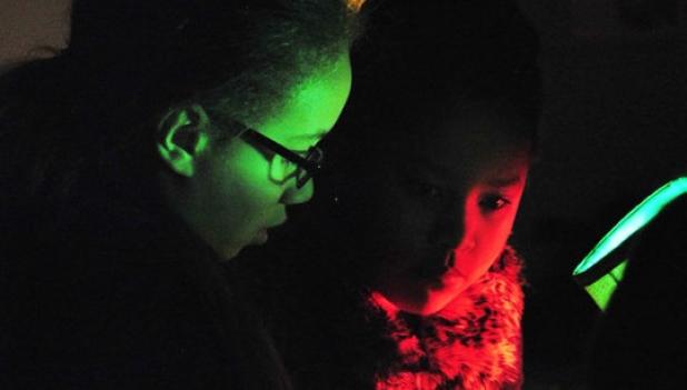 Joelle Spinks and Victoria Ventura, fourth graders at Martin Walker Elementary School, use a black light to search for clues on a piece of paper containing a sentence with comma splices. 