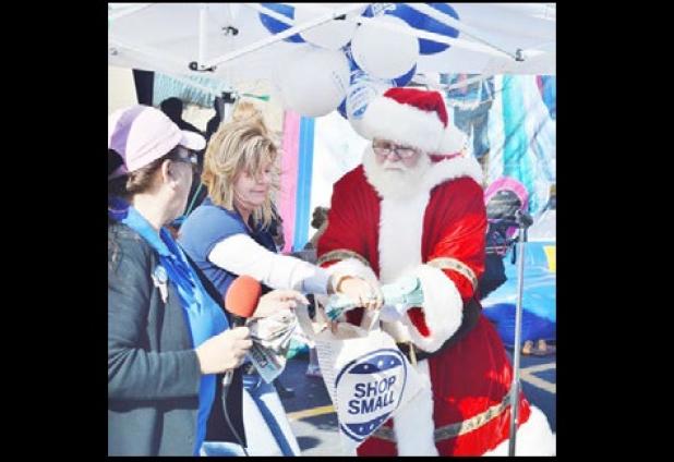 Santa draws a winning ticket for a $25 American Express gift card at the Small Business Saturday kickoff party in the Cove Terrace Shopping Center.